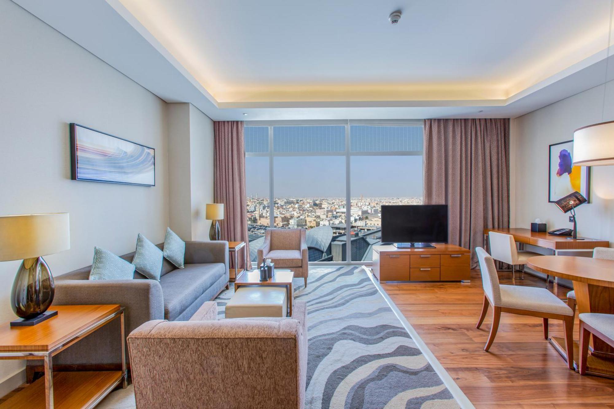 Hilton Riyadh Hotel & Residences Eksteriør bilde The photo shows a modern hotel room or suite. The space features a stylish living area with a sofa and armchairs arranged around a coffee table. There are lamps providing ambient lighting, and a large window offers a view of the cityscape outside. A 