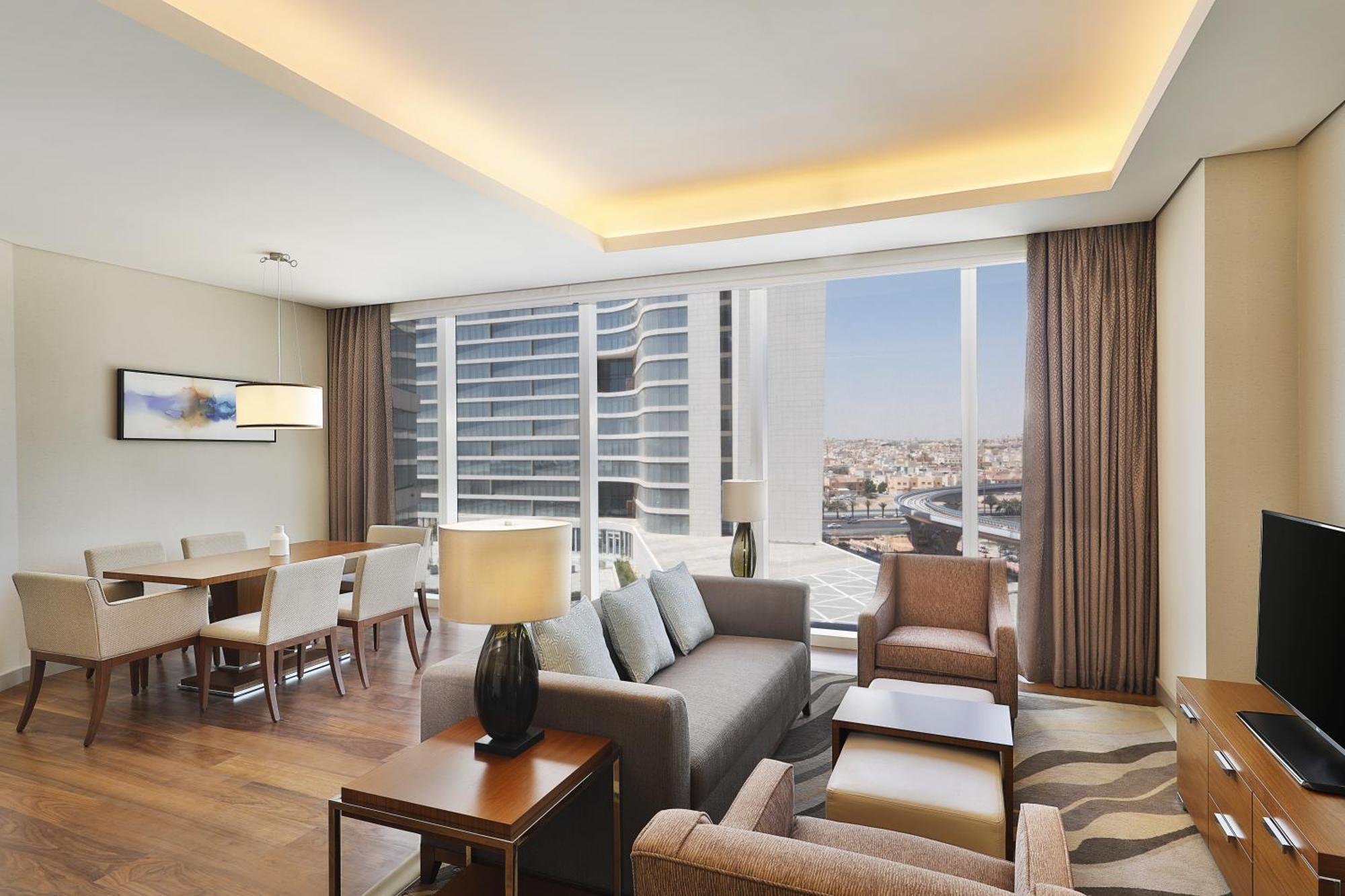 Hilton Riyadh Hotel & Residences Eksteriør bilde The photo shows a modern and stylish interior of a living space. The room features a comfortable seating area with a light gray sofa and two armchairs, complemented by a wooden coffee table. There is a desk and some furniture along the walls. Large w
