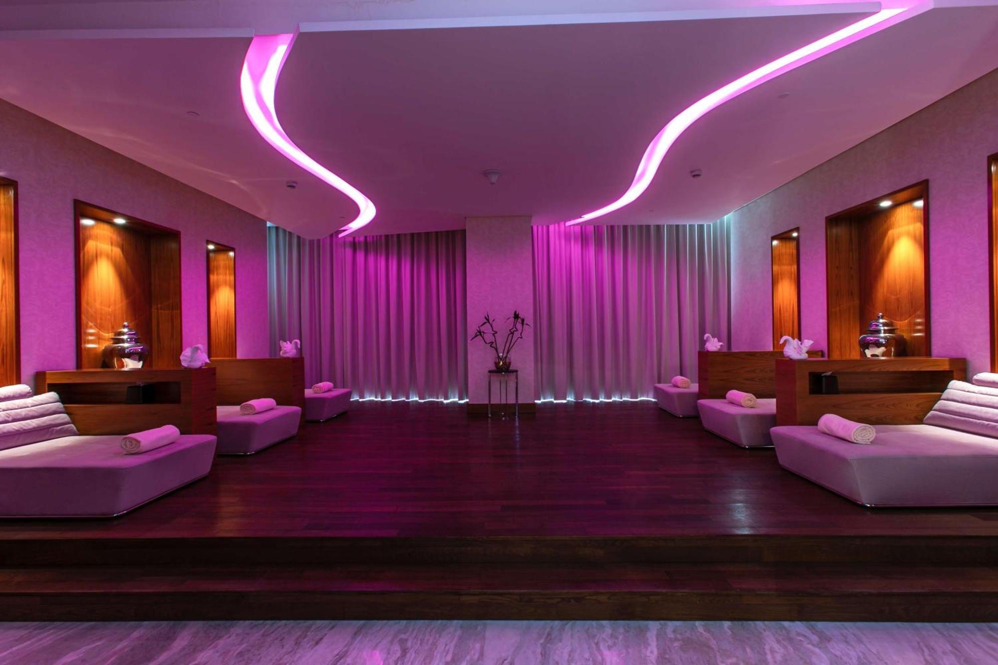 Hilton Riyadh Hotel & Residences Eksteriør bilde The photo depicts a relaxing interior space, likely a spa or wellness area. It features a wooden floor with a raised platform accented by soft, low couches on either side. The walls are adorned with modern lighting, which emits a calming pink hue. Th