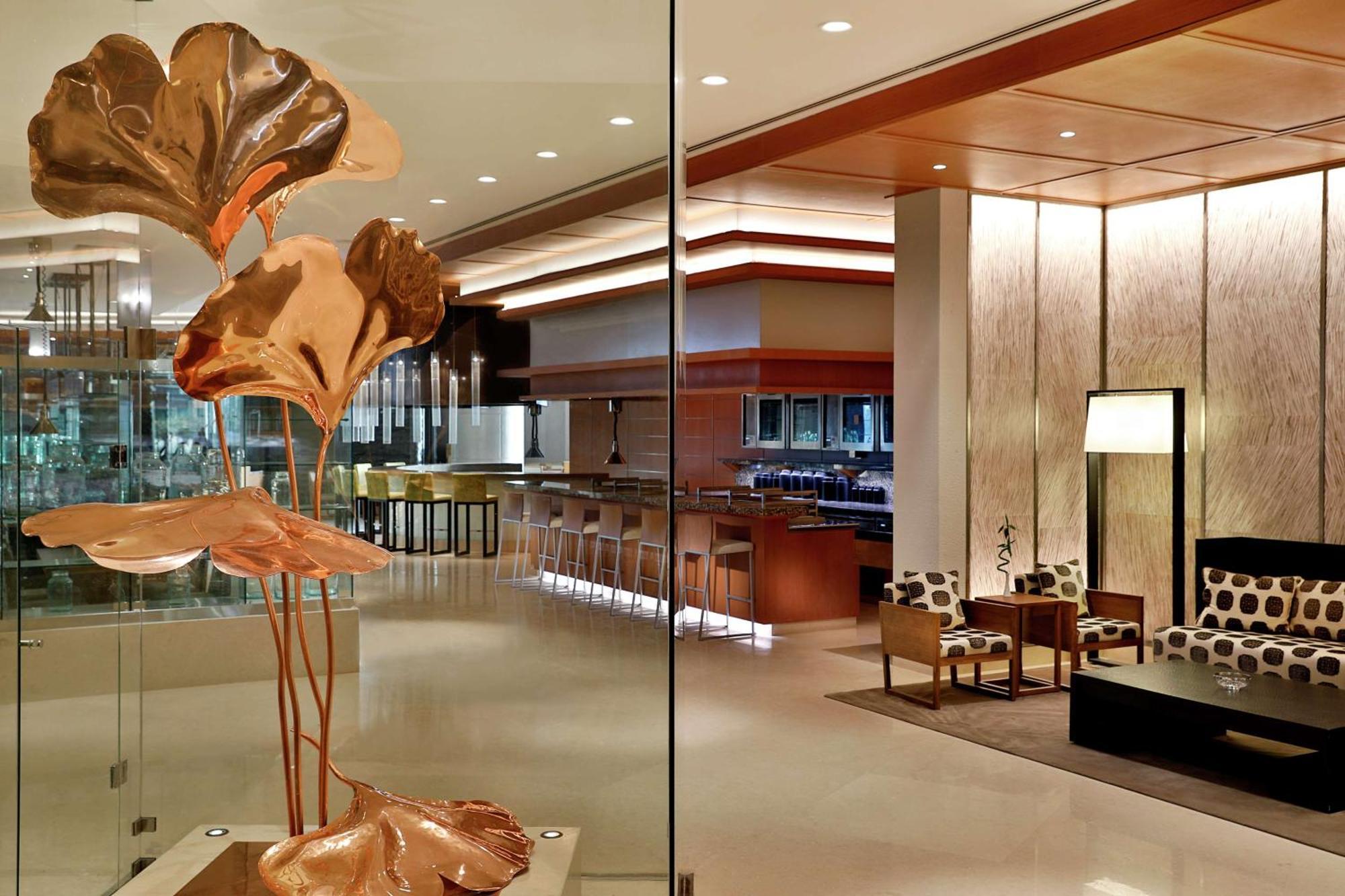 Hilton Riyadh Hotel & Residences Eksteriør bilde The photo depicts a modern and stylish interior space, likely a hotel lobby or upscale lounge. In the foreground, there is an artistic sculpture of copper-colored leaves or flowers, adding an elegant touch. The background features a well-lit bar area