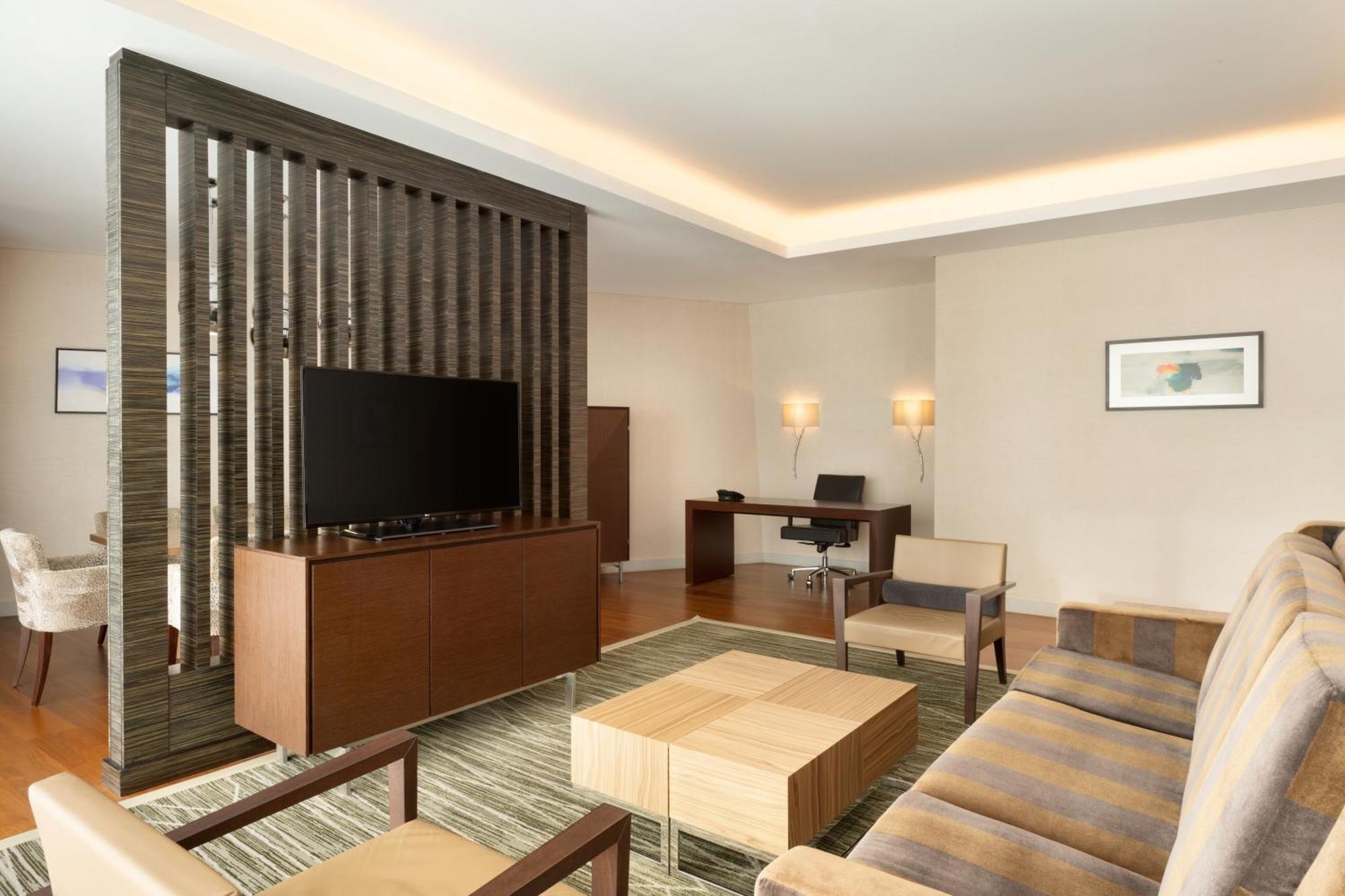 Hilton Riyadh Hotel & Residences Eksteriør bilde The photo shows a modern living space that features a contemporary design. It includes a seating area with a beige sofa and two armchairs arranged around a square wooden coffee table. A wall-mounted flat-screen TV is positioned on a decorative wooden