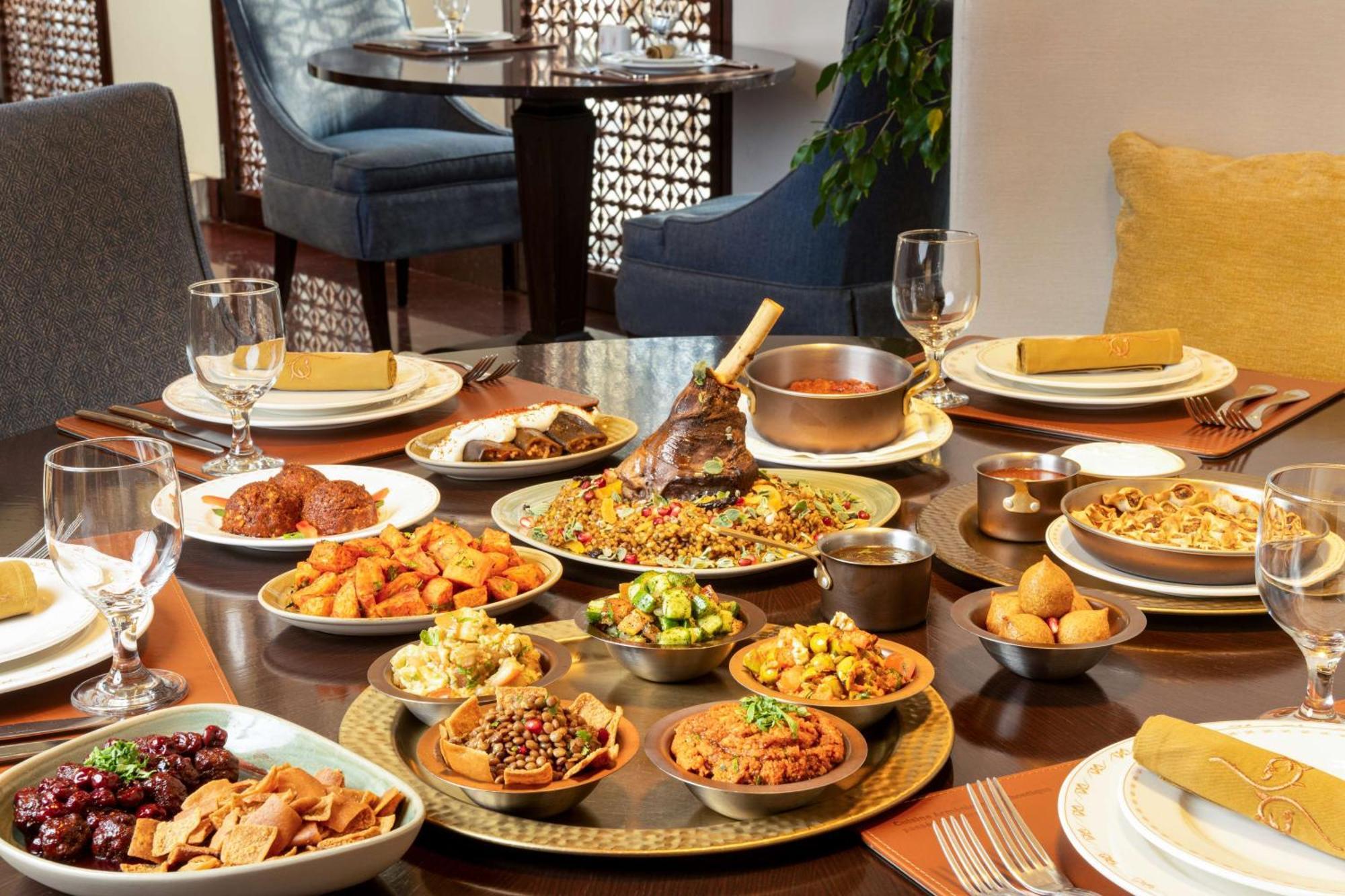 Hilton Riyadh Hotel & Residences Eksteriør bilde The photo depicts a beautifully arranged dining table featuring a variety of dishes. There are several large plates filled with different foods, including a prominent dish at the center that appears to be rice and meat, likely a type of biryani or pi